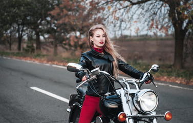 Plakat Beautiful biker woman posing outdoor with motorcycle on the road. 