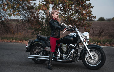Naklejka na ściany i meble Beautiful biker woman posing outdoor with motorcycle on the road. 