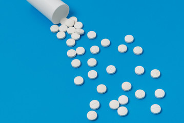 White tablets and bottle for tablets on blue background
