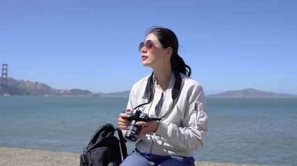 professional photographer holding slr camera sitting on rock zooming up picture photo. smiling girl tourist enjoy beautiful sunny day nature view sightseeing golden gate bridge san francisco usa. - Powered by Adobe