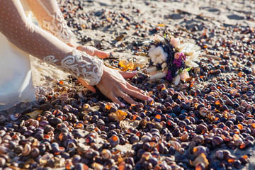 Hands of a bride playing with snail shells on the beach