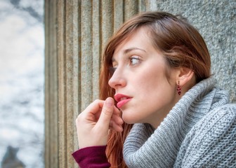 Bella ragazza dai capelli rossi che guarda fuori dalla finestra