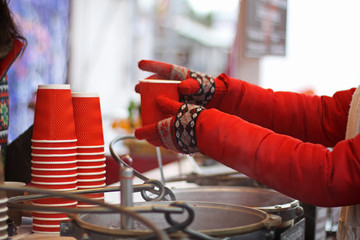 Female hands in red mittens, holding steaming cups, coffee, cocoa, mulled wine or tea, open. The concept of winter time. Bask in the cold. Women's hands in mittens hold a paper cup with a drink