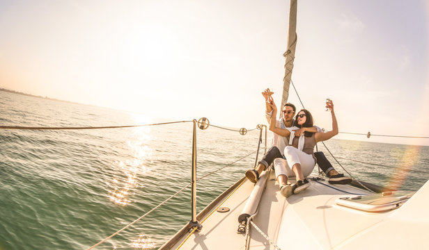 Young lovers couple on sail boat with champagne at sunset - Exclusive luxury concept with rich millennial people lifestyle on tour around the world - Soft backlight focus on warm sunshine filter