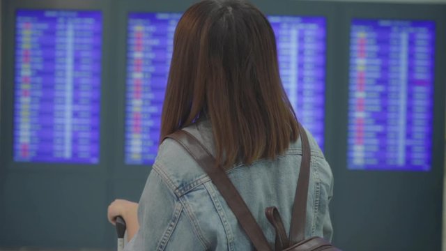 Slow motion - Happy Asian woman looking at information board checking her flight with luggage in terminal hall at the departure gate in international airport. Lifestyle women happy in airport concept.
