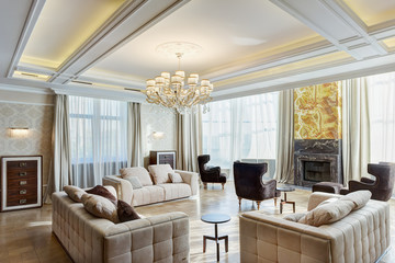 View of stylish and light living room with fireplace, big windows and crystal chandelier in center...