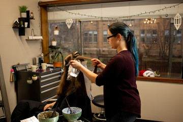 Hair color application by a young female hair stylist in a salon for education or website