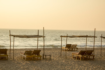 beach loungers under palm canopies on the sand against the ocean in the evening