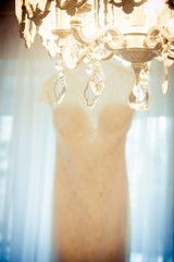 Brides wedding dress hanging near chandelier