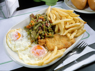 Plato con lomo y dos huevos fritos, verdura salteada y patatas fritas.