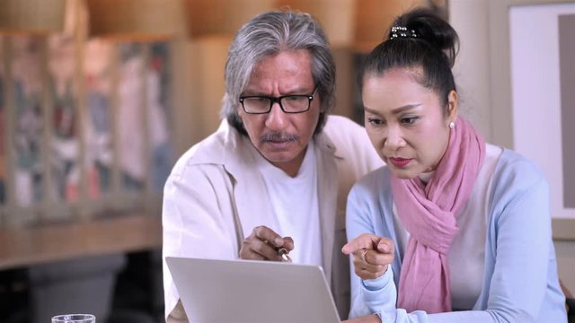 Senior Asian Couple working freelance small business entrepreneur SME  connected on laptop computer at home. Family business and technology concept.  Slow Motion