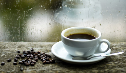 Autumn cloudy weather better with caffeine drink. Enjoying coffee on rainy day. Coffee morning ritual. Fresh brewed coffee white mug and beans on windowsill. Wet glass window and cup of hot coffee