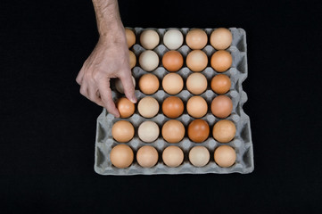 Male hand taking one egg from cardboard egg box on black mat background