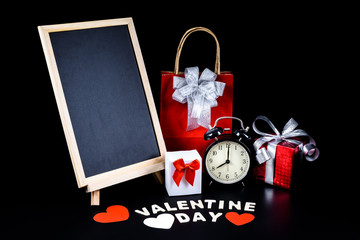 Chalkboard on stand, Heart shape, Gift box, alarm clock and Wooden letters word "VALENTINE DAY" on black background