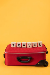 travel bag and wooden cubes with travel lettering on yellow background