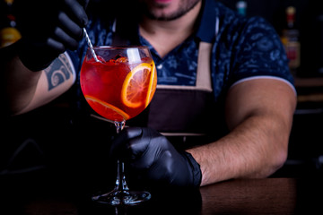 Expert barman is making cocktail at night club. Professional bartender at work in bar pouring sweet drink into glass on party at night club. Barman is decorating cocktail.