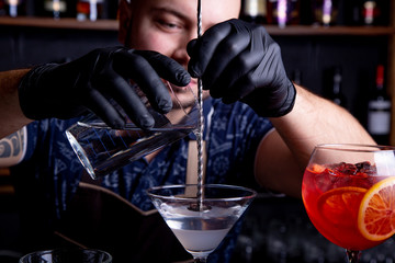 Expert barman is making cocktail at night club. Professional bartender at work in bar pouring sweet drink into glass on party at night club. Barman is decorating cocktail.