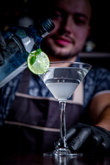 Expert barman is making cocktail at night club. Professional bartender at work in bar pouring sweet drink into glass on party at night club. Barman is decorating cocktail.