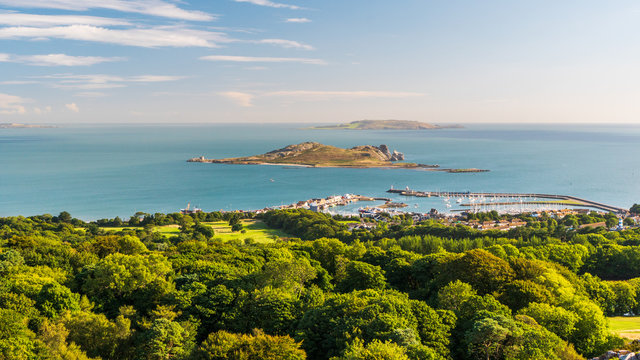 Irish landscape as seen from the Ben of Howth with green trees, turquoise sea waters and Ireland's Eye Island in the distance on a beautiful summer day.