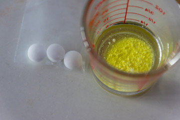 Yellow powder pill with water in glass and 3 tablets pills in plastic bag for patient.