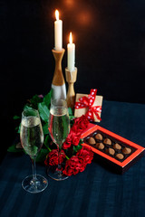 Two glasses with champagne and a bouquet of red roses and candies on the background of candles