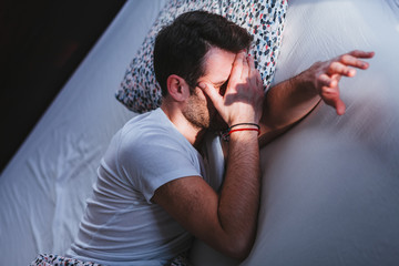 Young tired man waking up in bed in the morning