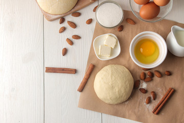 baking ingredients. baking tools. dough with butter, eggs, sugar, milk, cinnamon, almonds on a white wooden background. view from above. space for text