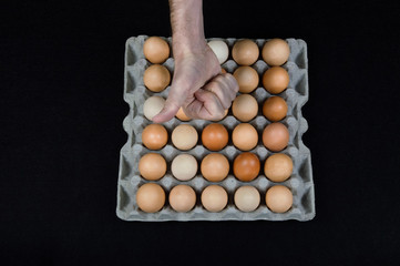 Male hand showing thumb up over a carton box full of hen eggs on black mat background
