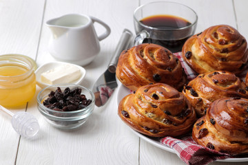 Tasty buns with raisins and coffee with milk on a white wooden background. fresh bakery. breakfast.
