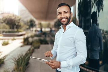 Portrait of a young confident smiling indian man holding a tablet and looking into the distance