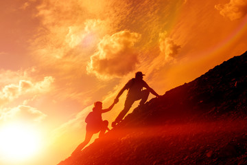 silhouette of a man and a girl rising to the top of the mountain at sunset. conquest of the top, friendship. help