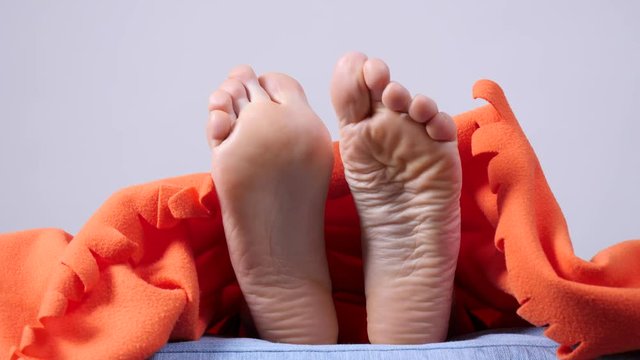 Human feet moving on the bed under orange blanket, slow motion