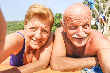 Senior happy couple taking selfie at beach resort in Thailand trip on tropical tour - Adventure and fun concept of active elderly around the world - Hot sunny day with warm saturated filtered tones