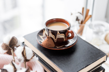 Cup of coffee with milk on the books near the window, a sprig of cotton