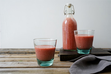 Strawberry banana smoothie in glasses and bottle. Rustic wooden table, white background