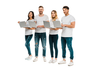 Obraz premium happy young men and women standing with laptop and smiling at camera isolated on white