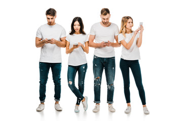 Obraz premium full length view of young friends in white t-shirts and jeans using smartphones isolated on white