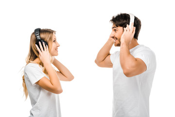side view of young couple listening music in headphones and smiling each other isolated on white