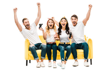 Fototapeta premium excited young friends sitting on couch and playing with joysticks isolated on white