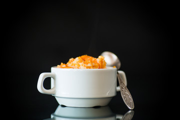 sweet boiled pumpkin porridge with rice in a plate on a black