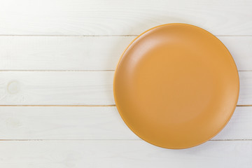Directy above Empty yellow matte plate on white wooden background with copy space
