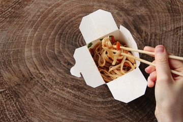 Udon Japanese noodle. female hand using chopsticks. wok with chicken and vegetables