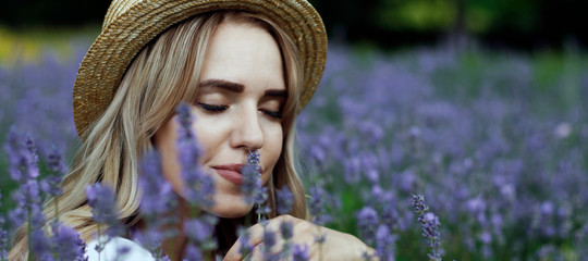 Blonde girl in a straw hat in a lavender field, closing her eyes inhales the scent of flowers