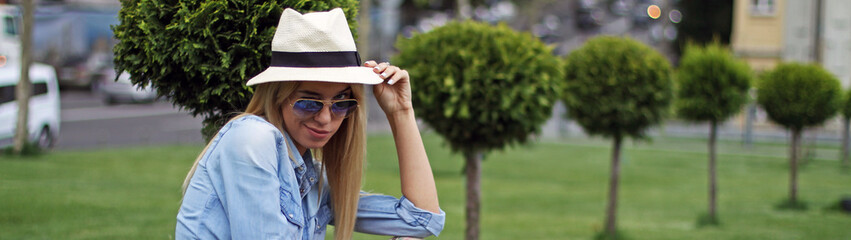 The girl the blonde in the hat beautifully smiling sitting on the summer green lawn