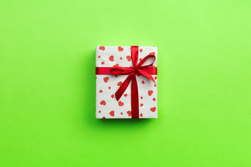 Gift box with red ribbon and heart on green background, top view with copy space for text
