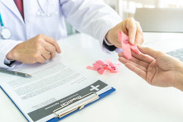 close up hand of Doctor Holds Pink Ribbon given to woman patient while talking raising knowledge with tumor illness. Concept of Pink ribbon for breast cancer awareness or October Pink day,health care