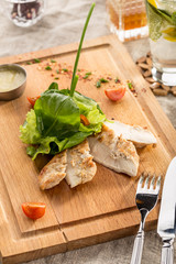 Grilled chicken breasts and green salad served on wooden board on the table