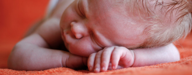 A newborn baby sleeping on his stomach, put his hands under his head