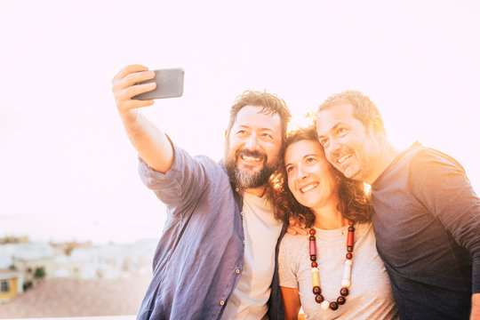 Bright yellow filter group of caucasian 40 years old people men and woman taking selfie picture with smart phone device - backlight and white sky in bnackground - happy leisure activity toncept
