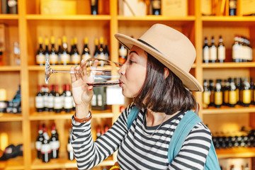 Happy asian Woman sniffing and tasting red wine in a glass in winery shop